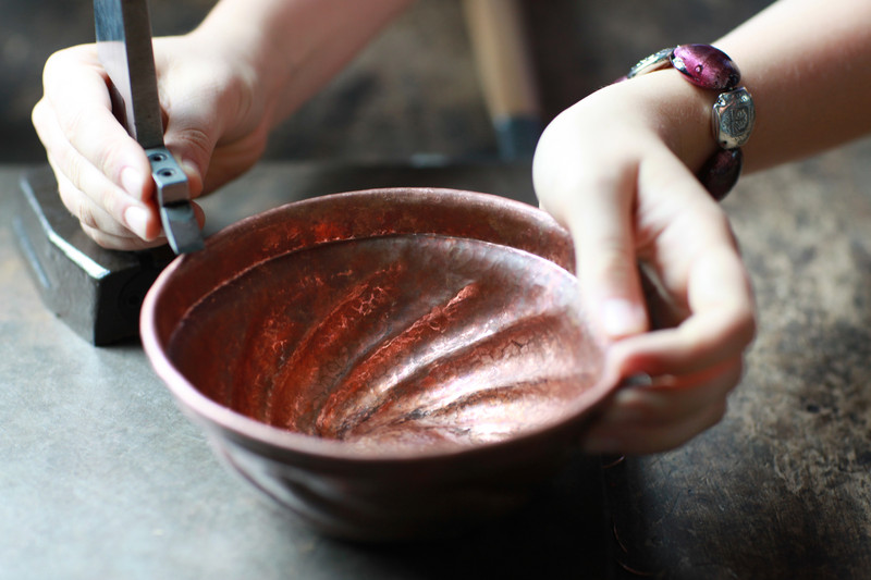 Hands work on a copper bowl
