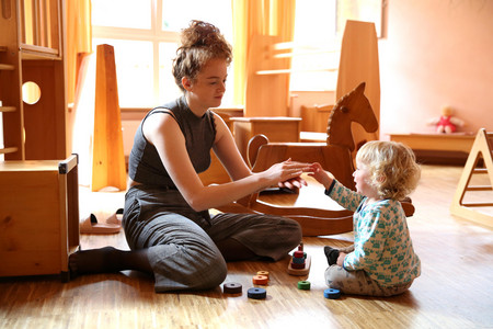 Teacher with child playing in the dollhouse; in the background a rocking horse