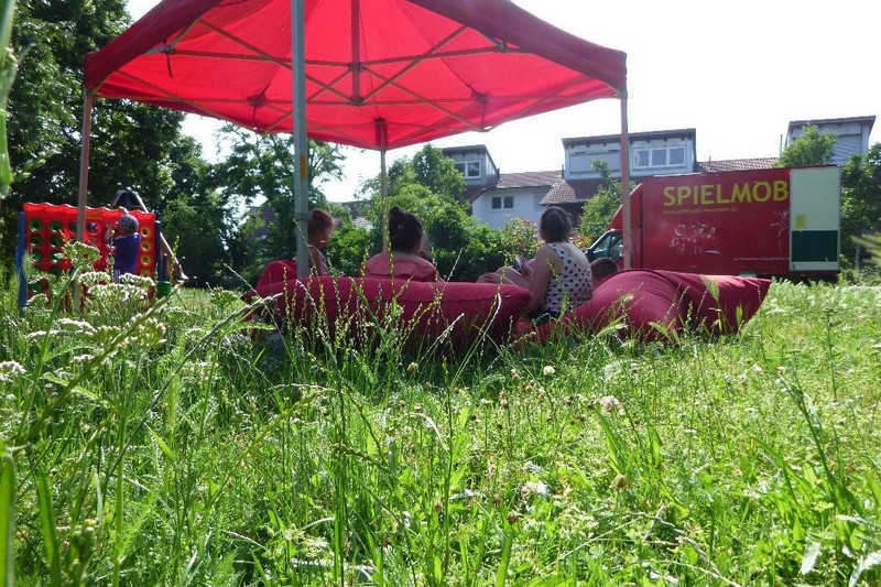 Kinder unter Sonnenschirm vor dem Spielmobil