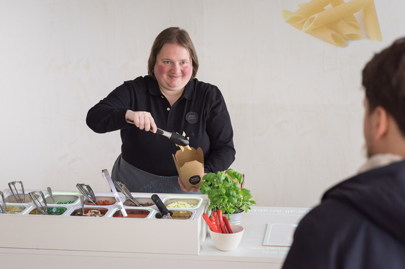 A staff member preparing noodles for a customer