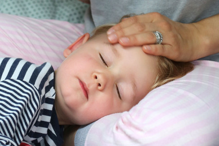 Fieberndes Kind mit Hand der Mutter auf der Stirn