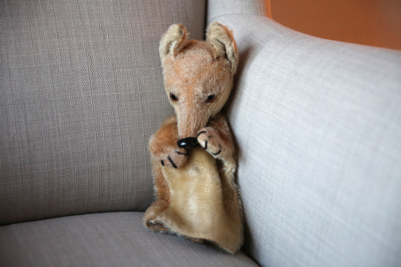 In der Ecke eines Sofas sitzt als Handpuppe ein Fuchs, der durch seine gesenkte Kopfhaltung schüchtern wirkt.