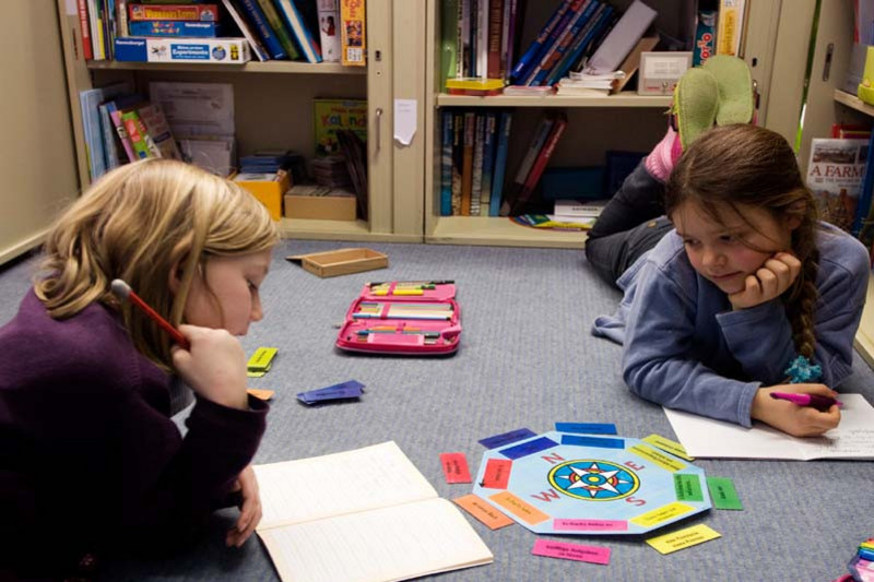 Two young girls learning while lying on the flor