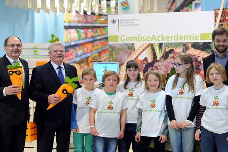 Gruppenfoto mit Bundespräsident Joachim Gauck, Landwirtschaftsminister Christian Schmidt und Kindern, die alle das Maskottchen der GemüseAckerdemie, eine Karotte mit Brille, in Händen halten 