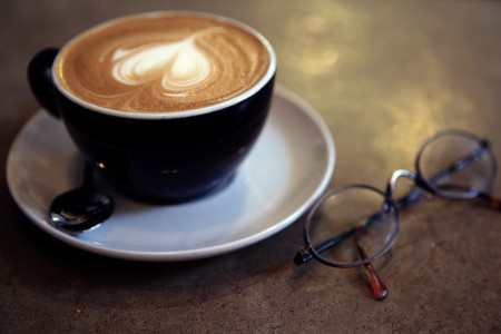 Tasse Kaffe mit Herzschaum und Lesebrille