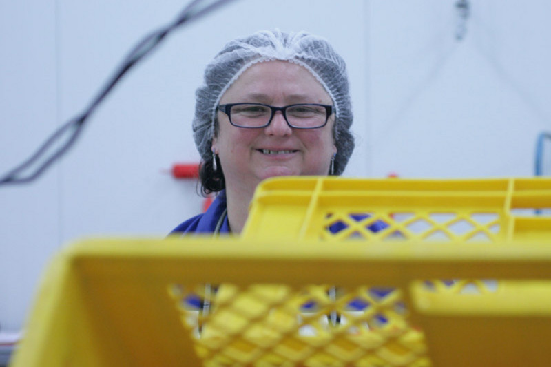 An employee with a hairnet is carriing a yellow box