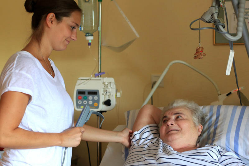 Eine Krankenschwester steht am Bett einer Patentin, beide lächeln
