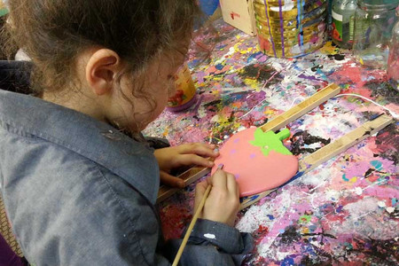 In a painting workshop a young girl is painting a wooden strawberry