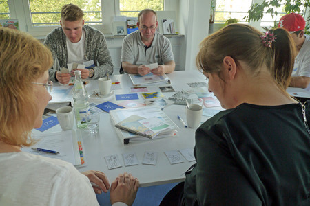 Vier Menschen sitzen an einem Tisch mit Lehrmaterialien und unterhalten sich
