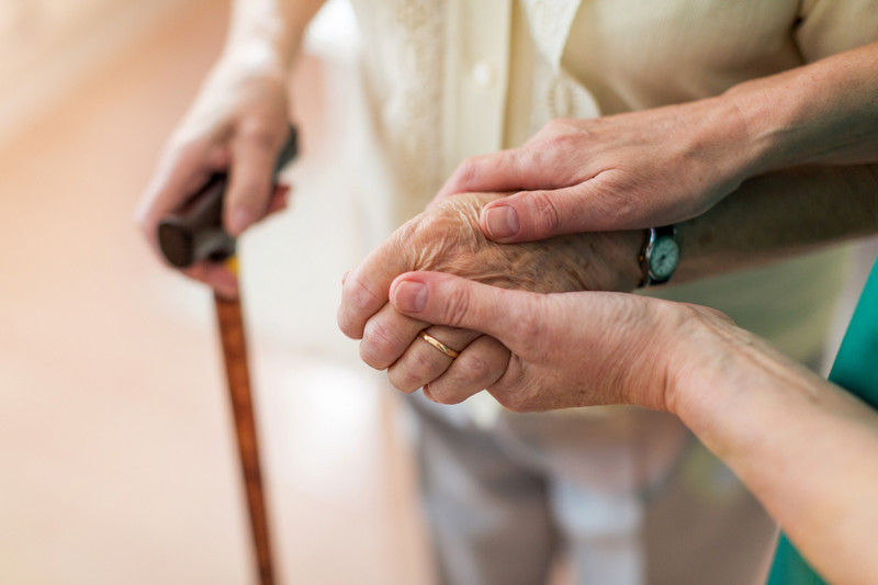 Helping hands: carer looks after old woman with walking stick