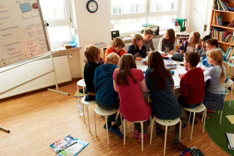 Schüler sitzen beim gemeinsamen Lernen auf Hockern um einen Tisch