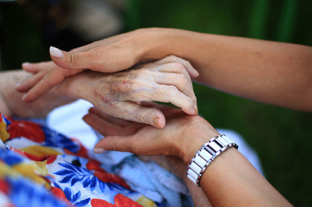 Hands of a young woman holding the hand of an older woman