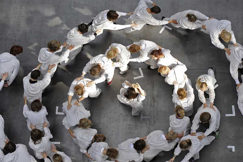 Youths in white costumes walking in circles, each with his or her hands on the sholders of the person in front