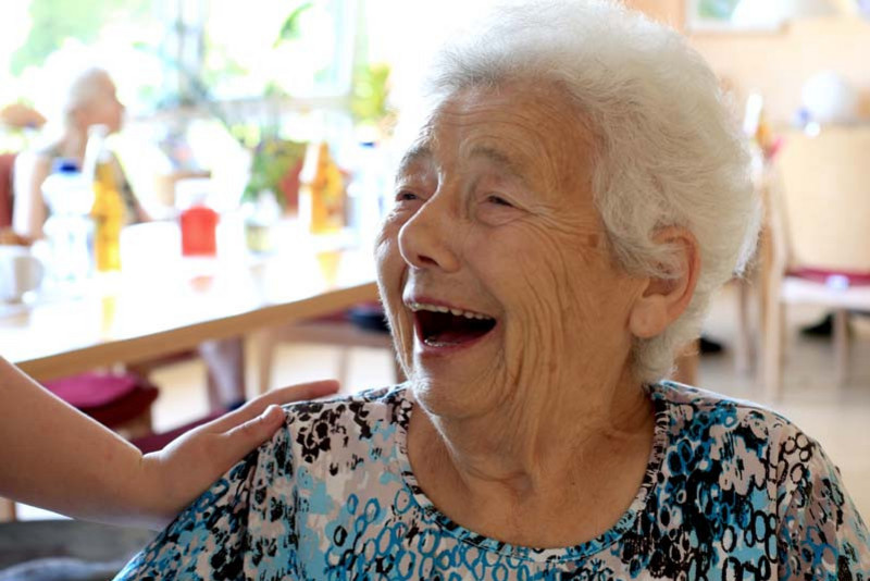 Eine herzlich lachende alte Frau im Gemeinschaftsraum