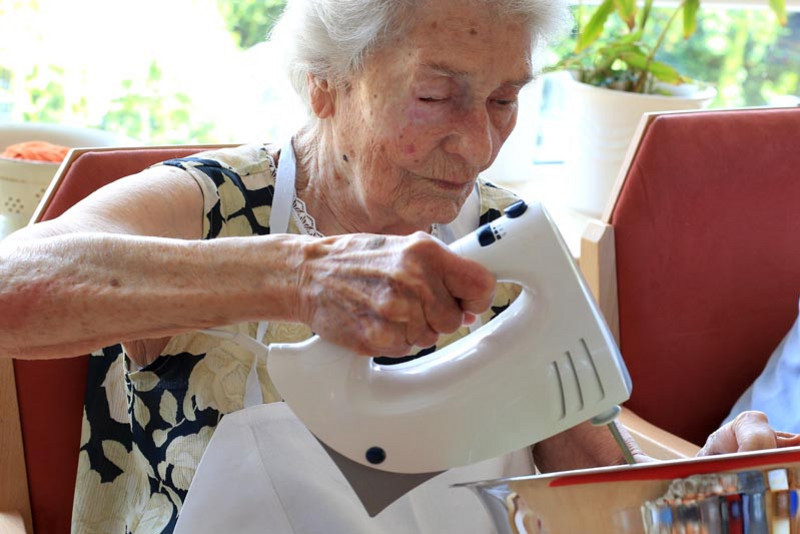 Eine alte Frau mit einem Rührgerät in der Hand hilft beim Backen