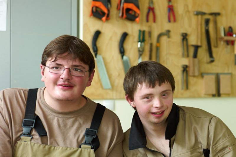 Two teenagers in work clothes in front of a workbench