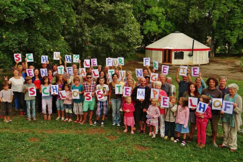 Children and adults holding papersheets with colourfull letters, saying 'school for free development Schloss Tempelhof'