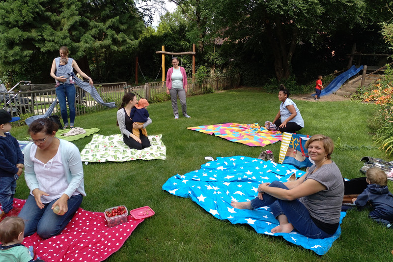 Mothers play on blankets in the garden with their toddlers