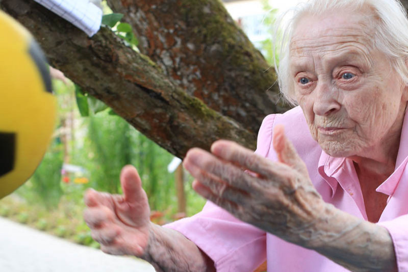 Eine alte Frau steht im Garten und wirft einen Ball 