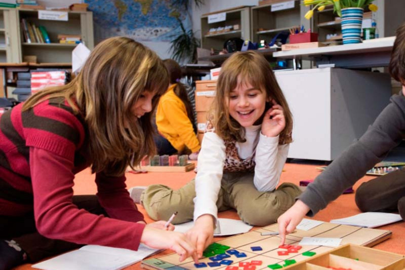 Schülerinnen sitzen mit einem Lernspiel auf dem Boden des Klassenzimmers