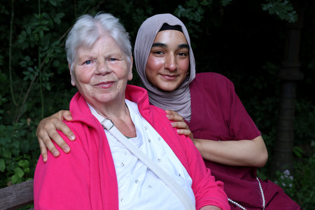 Junge Pflegerin mit Kopftuch an der Seite einer älteren Frau