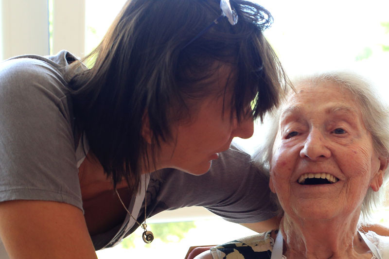 A care taker puts her arm around an older woman