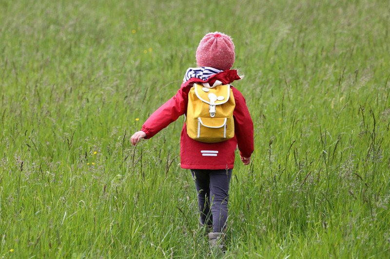 Kind mit Rucksack streift durch Wiesen