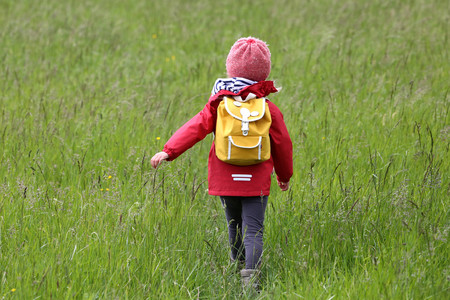 Child with backpack roaming through meadows