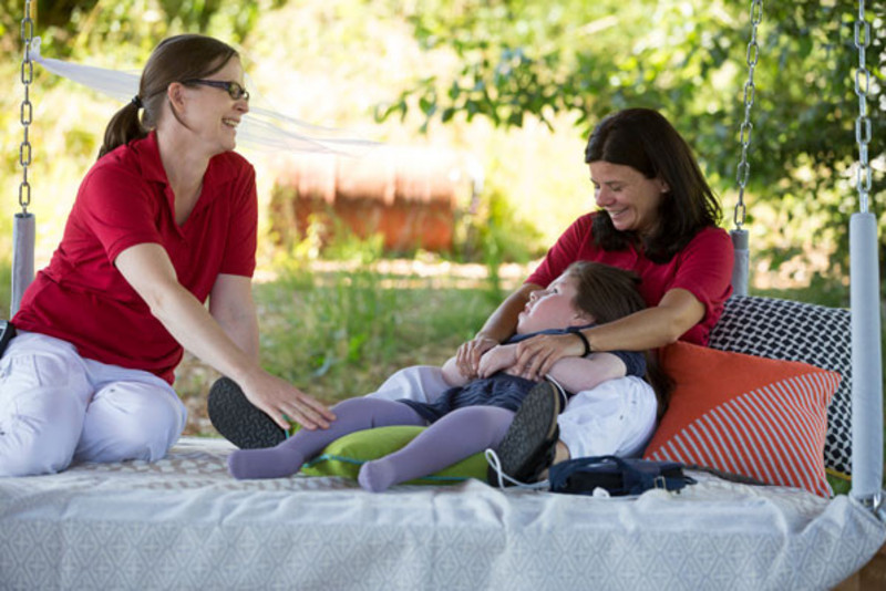 Two caretakers and a child on a big hollywood swing in the garden