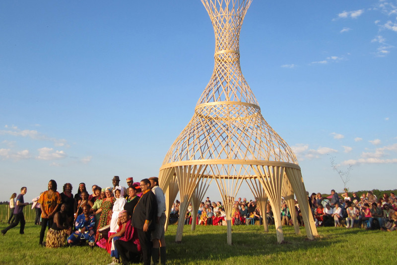 Goup photo of participants in front of the sculpture in the evening sun