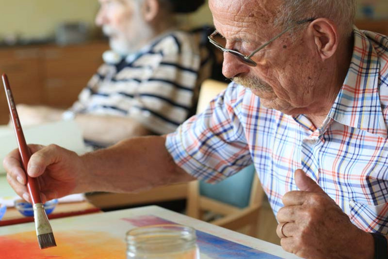 Ein alter Mann malt mit Pinsel und Farben