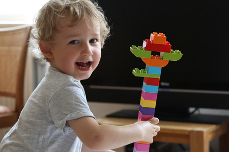 Boy plays laughing with building blocks in front of a switched-off TV